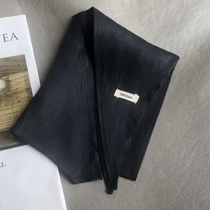 Detail shot of the 100% linen material label on a premium black triangular scarf