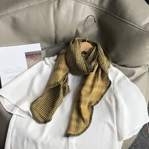 Detailed view of green and mustard plaid cotton scarf on a wooden hanger with white shirt