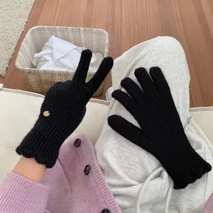 Detail of black knit gloves featuring a wavy cuff and decorative gold metal button accent