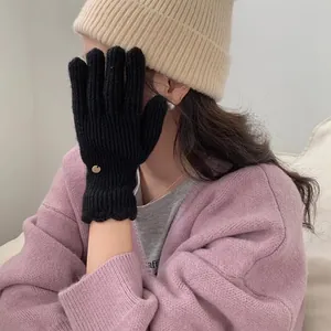 Detail of black knit gloves with wavy cuffs and small gold charm on winter attire