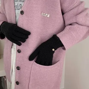 Detail of thick black knit gloves featuring metallic emblem decoration on female model