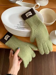 Detail of avocado green knit gloves with brown ribbed cuffs and white fabric brand label