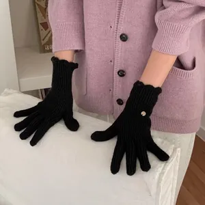 Detail of black knitted gloves with wavy cuffs and a gold charm on soft fabric