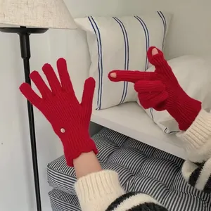 Detail of red knit gloves with pearl accents and functional openings for touchscreens
