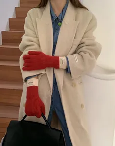 Close-up of red knitted gloves with white ribbed cuffs and a decorative label detail