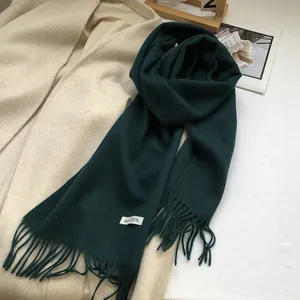 Detailed close-up of dark green 100% Australian wool scarf with tassels and material label