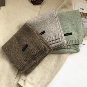 Three premium 100% wool knitted scarves in brown, grey, and green laid on a coat