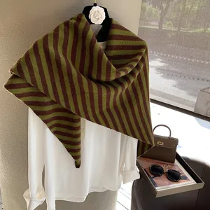 Detalle del chal triangular de lana a rayas verdes y marrones sobre una camisa blanca