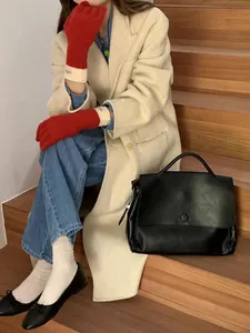 Close-up of touchscreen knit gloves paired with a beige wool coat and leather handbag