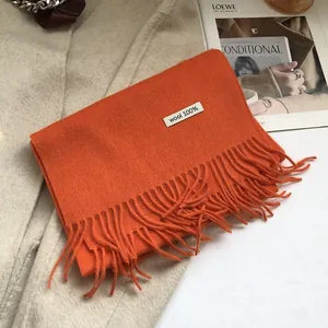 Detail of bright orange 100% wool scarf with thick fringe on a wool coat background