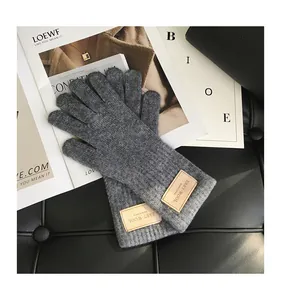 Nahaufnahme dunkelgrauer Strickhandschuhe aus Wolle mit edlem braunem Leder-Logo-Patch