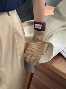 Detail of color-block knit gloves with warm beige and coffee brown tones and woven label