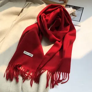 Detail of red 100% Australian wool scarf with tassels on cream coat background