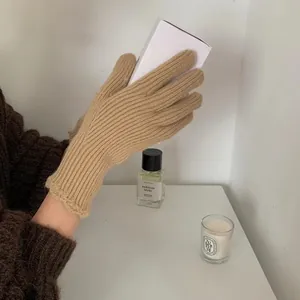 Detail of beige chunky knit glove with scalloped cuffs holding a white gift box
