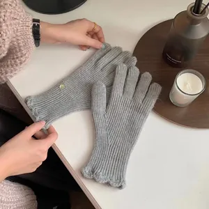 Detail of grey knitted wool gloves with ruffled cuffs and subtle green embellishment