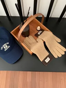 Close-up of khaki knit gloves with ribbed texture and woven label in a wooden tray