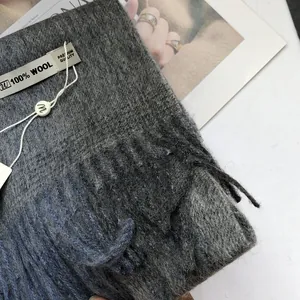 Detail eines Schals aus 100% Wolle mit graublauem Farbverlauf, Fransen und Etikett