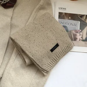 Detail of 100% wool speckled scarf in oatmeal with knit texture and material tag