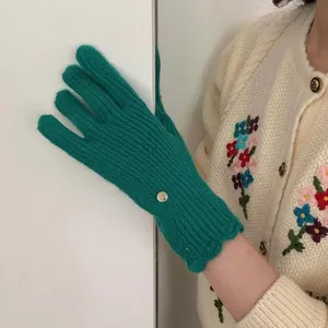 Detail of green ribbed knit glove with gold metal tag and elegant scalloped edge