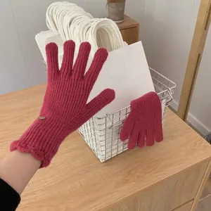 Close-up of rose red ribbed knit gloves with ruffled cuffs and metallic trim detail