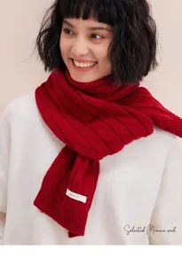Detail shot of chunky red knit scarf with cable pattern and 100% wool material label