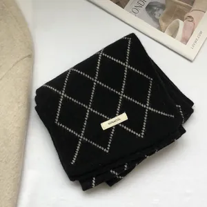 Detailed view of the 100% wool label on a black and beige diamond pattern knit scarf