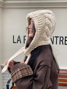 Detail of chunky cable-knit balaclava hat in cream with long decorative straps