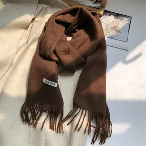 Detailed macro of a dark brown wool scarf featuring tassels and a 100% wool material label