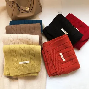 Close-up of thick cable knit 100% wool scarves in various colors with a 100% wool label