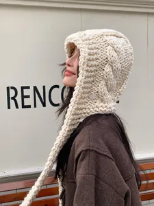 Detail of chunky cable-knit cream balaclava featuring long braided tassels and soft texture