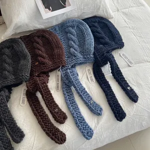 Thick chunky knit trapper hats with long earflaps in four colors on a bed