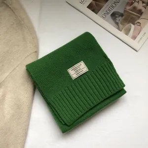 Detailed view of green 100% wool scarf featuring a ribbed knit texture and fiber label