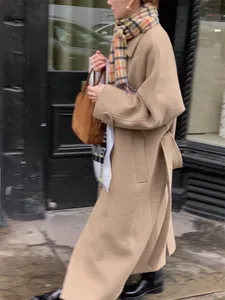 Detail view of a long camel wool coat with side slits and a matching belted waistline