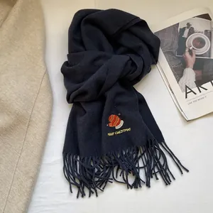 Detail of navy knit scarf with Merry Christmas embroidery and soft fringe edges