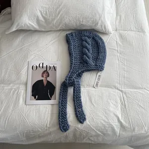Detailed close-up of blue chunky knit balaclava with heart metal charm and side ties