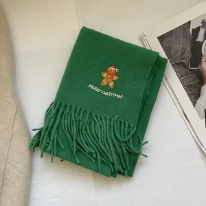 Detail of green Christmas scarf featuring gingerbread man embroidery and soft fringe trim