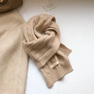 Close-up of beige cable knit 100% wool scarf showing texture and material label
