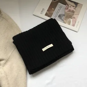 Close-up of 100% wool black ribbed scarf with minimalist white material label
