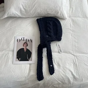 Detail of navy blue chunky knit earmuff hat with cable pattern and metal heart charm