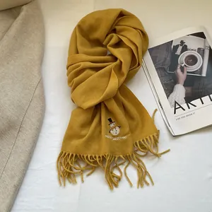 Detail of ginger yellow knitted scarf with snowman embroidery and tassel fringe