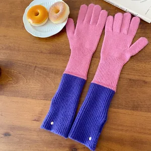 Detailed view of long pink and purple knit gloves with thumb holes on a wooden table