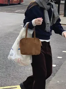 Minimalist dark brown suede handbag with thin handles shown in a lifestyle street setting