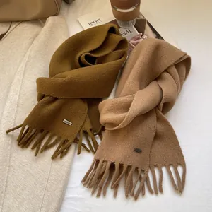 Close-up of soft 100% wool knit scarves with long tassels and delicate metal logo detail