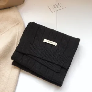 Close-up of 100% pure wool black cable-knit scarf showing premium texture and label