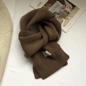 Detailed view of thick dark brown wool knit scarf with ribbed hem and decorative tag