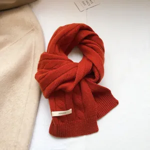 Close-up of 100% wool orange cable knit scarf with visible washing label and soft texture