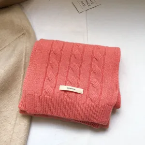 Macro shot of 100% pure wool scarf showing thick cable knit texture in coral pink