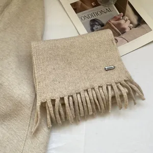 Detailed close-up of beige knitted wool scarf with long fringes and metal logo tag