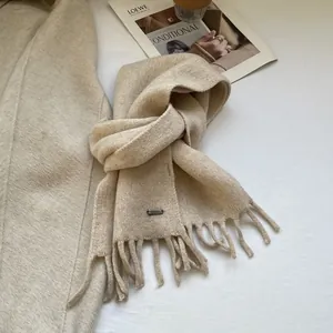 Detailed texture of beige wool knit scarf featuring classic fringe and metallic logo plate