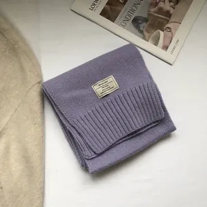 Detail of purple wool knit scarf with ribbed edge and woven label on a lifestyle layout